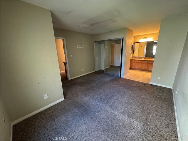 unfurnished bedroom featuring ensuite bath, light colored carpet, baseboards, and a closet