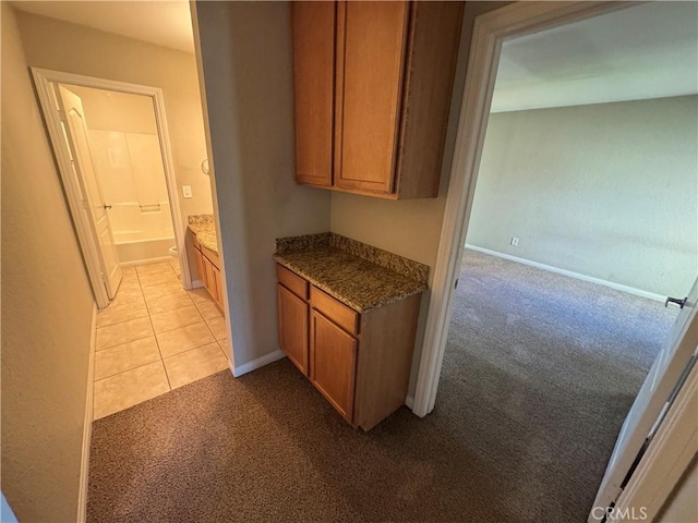 kitchen with light carpet, light tile patterned floors, brown cabinetry, and baseboards