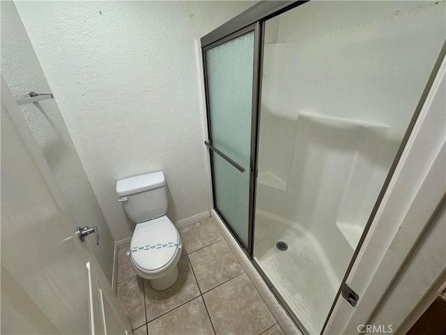 bathroom with tile patterned floors, a stall shower, toilet, and baseboards