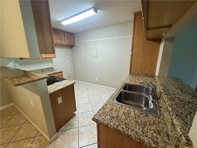 kitchen with a sink, a peninsula, brown cabinetry, light tile patterned floors, and baseboards