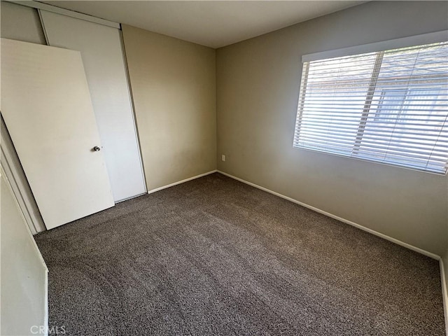 unfurnished bedroom with a closet, dark carpet, and baseboards