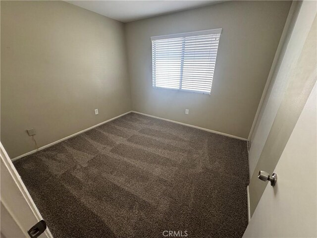 empty room with baseboards and dark colored carpet