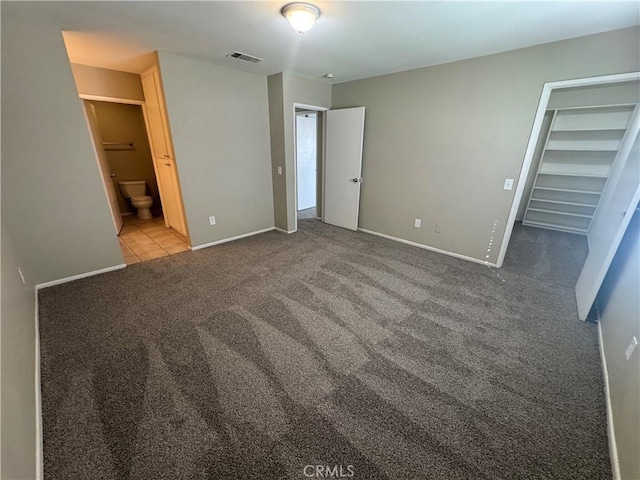 unfurnished bedroom featuring a spacious closet, visible vents, baseboards, carpet, and ensuite bath