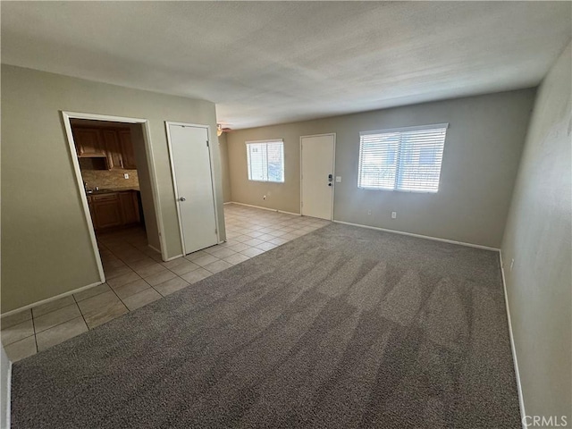 empty room featuring a textured ceiling, light tile patterned floors, baseboards, and light carpet