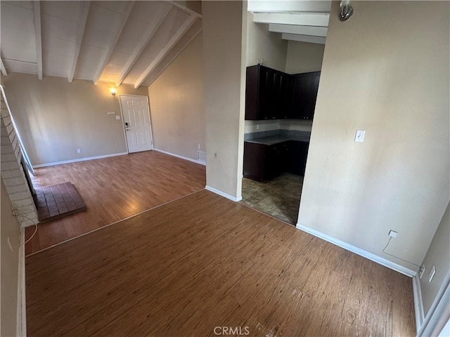 unfurnished living room with beam ceiling, wood finished floors, baseboards, and high vaulted ceiling