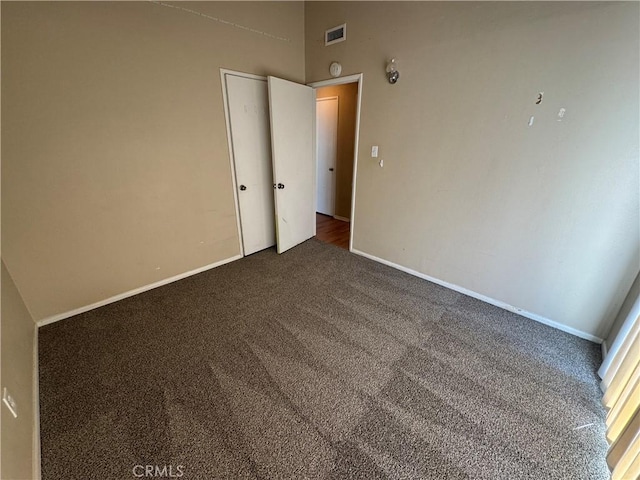 spare room with dark colored carpet, visible vents, and baseboards