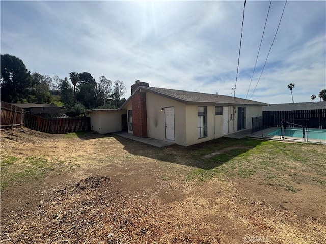 rear view of house featuring stucco siding, a fenced in pool, a fenced backyard, and a chimney