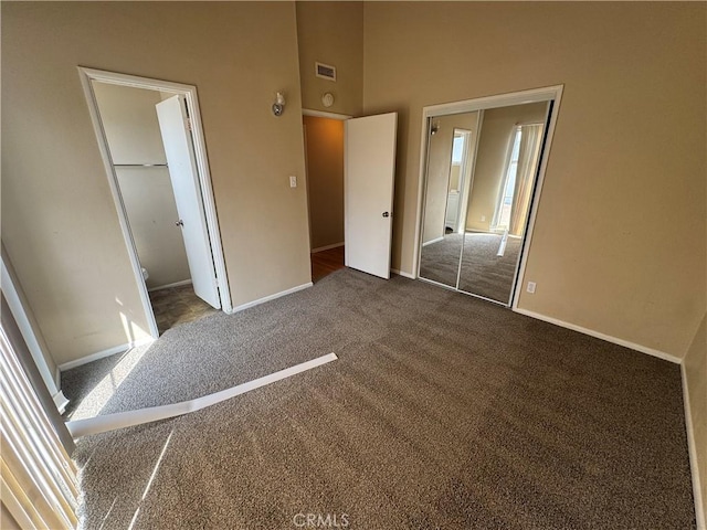 unfurnished bedroom featuring a closet, visible vents, dark carpet, and baseboards