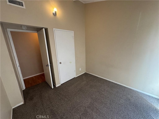 unfurnished room with visible vents, dark carpet, and baseboards