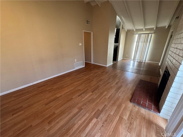 unfurnished living room with visible vents, baseboards, beam ceiling, a fireplace, and wood finished floors