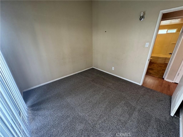 spare room featuring dark carpet and baseboards