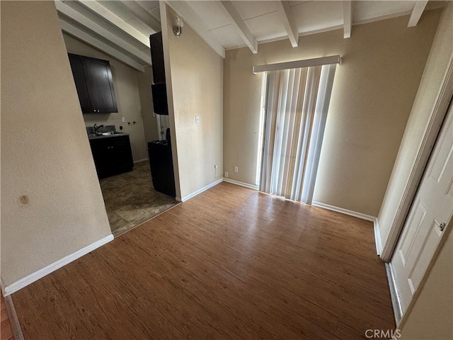 spare room featuring a sink, vaulted ceiling with beams, baseboards, and wood finished floors