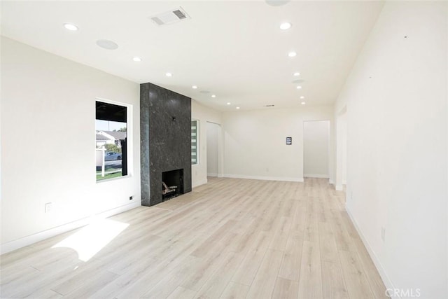 unfurnished living room with a high end fireplace, visible vents, recessed lighting, and light wood finished floors