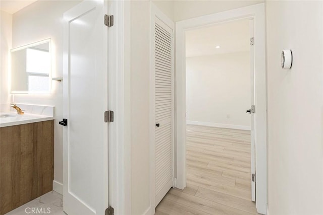 corridor featuring light wood finished floors, baseboards, and a sink