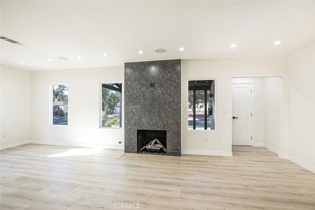 unfurnished living room with a high end fireplace, visible vents, plenty of natural light, and light wood-style flooring