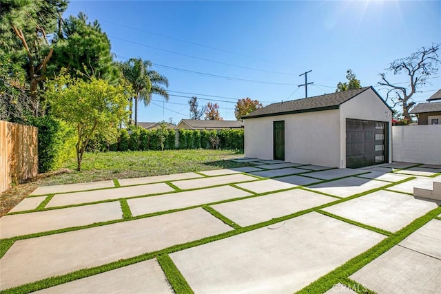 view of patio with an outbuilding, concrete driveway, fence, and a detached garage