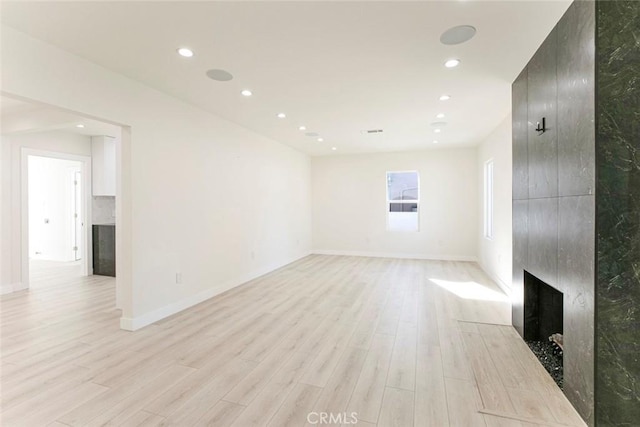 unfurnished living room with recessed lighting, baseboards, a large fireplace, and light wood-style floors