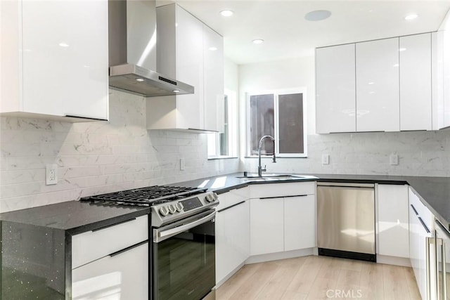 kitchen featuring appliances with stainless steel finishes, white cabinets, modern cabinets, wall chimney exhaust hood, and a sink