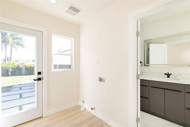 entryway with baseboards, visible vents, light wood finished floors, and a sink