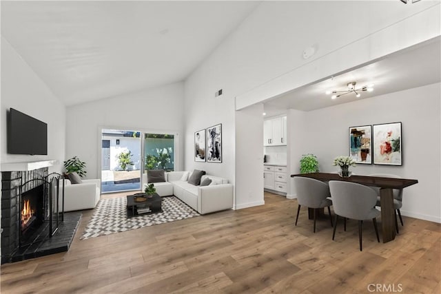 living area with light wood-type flooring, baseboards, high vaulted ceiling, and a brick fireplace