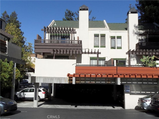 rear view of house featuring stucco siding, parking, a pergola, and a chimney