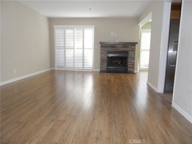 unfurnished living room with baseboards, a stone fireplace, and wood finished floors