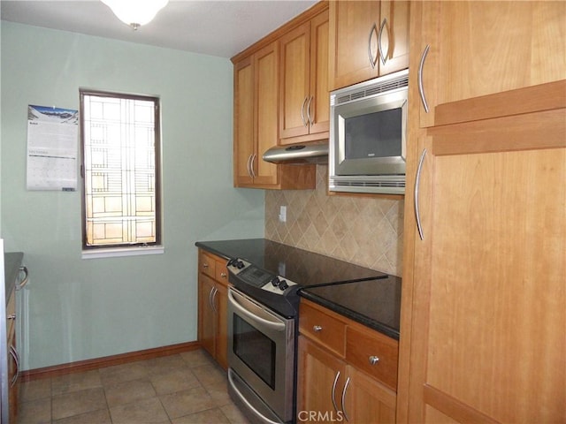 kitchen with brown cabinetry, stainless steel appliances, decorative backsplash, under cabinet range hood, and dark countertops