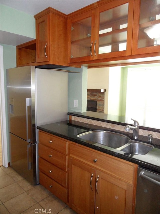 kitchen with glass insert cabinets, light tile patterned floors, brown cabinets, appliances with stainless steel finishes, and a sink