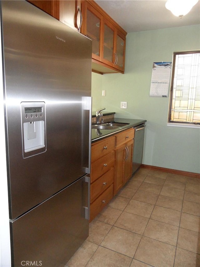 kitchen with light tile patterned floors, a sink, stainless steel appliances, dark countertops, and brown cabinets