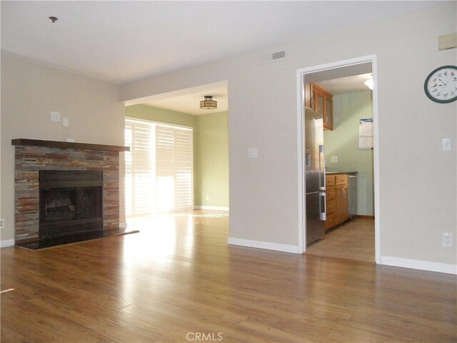 unfurnished living room featuring a fireplace with flush hearth, baseboards, and light wood-style floors