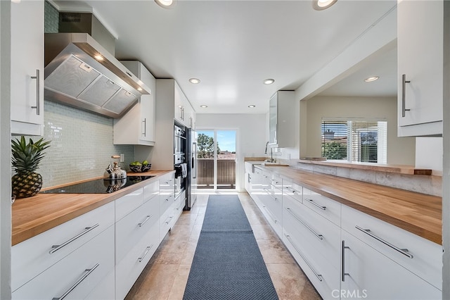 kitchen featuring black electric stovetop, wall chimney exhaust hood, tasteful backsplash, and wooden counters