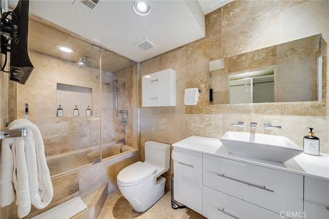 bathroom with visible vents, toilet, vanity, a combined bath / shower with rainfall shower, and tile walls