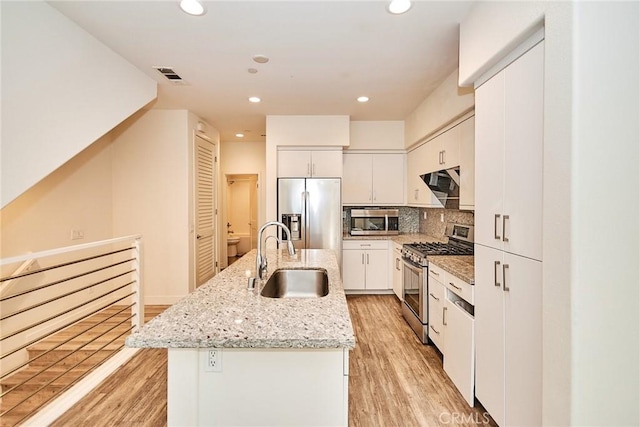 kitchen featuring a sink, stainless steel appliances, an island with sink, and light wood finished floors