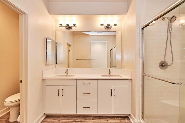 bathroom featuring a shower stall, toilet, double vanity, and a sink