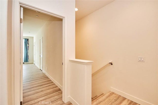 hallway featuring an upstairs landing, baseboards, and light wood finished floors