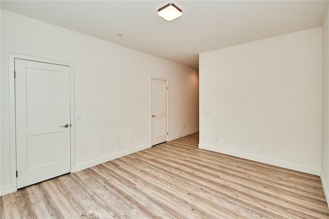 spare room with baseboards and light wood-style floors