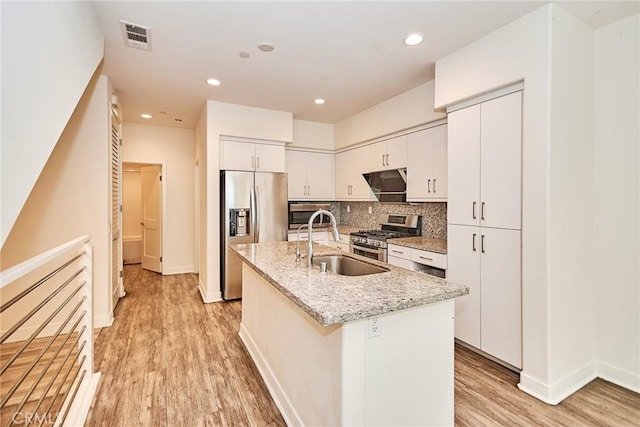 kitchen with visible vents, a kitchen island with sink, a sink, stainless steel appliances, and light wood-style floors