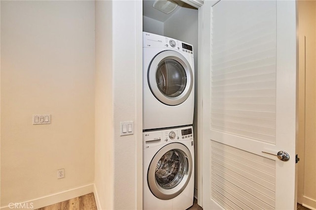 laundry room with laundry area, stacked washer / dryer, wood finished floors, and baseboards