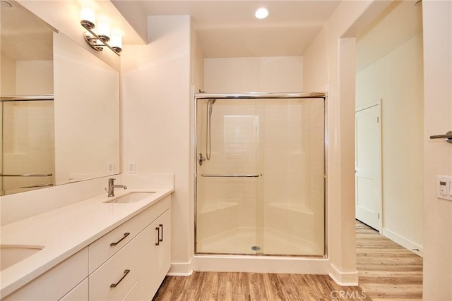 bathroom with a stall shower, a sink, wood finished floors, double vanity, and baseboards