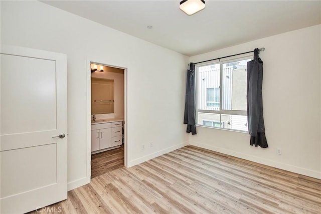 unfurnished bedroom with a sink, baseboards, ensuite bath, and light wood-style flooring