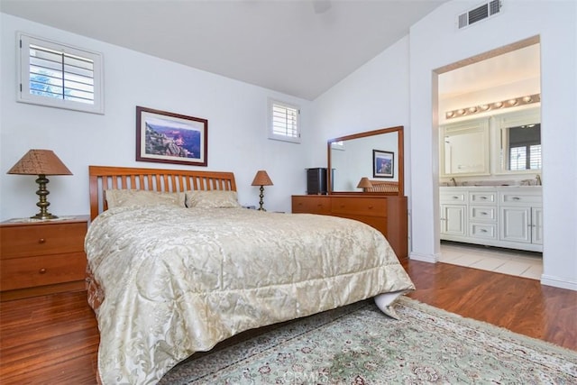 bedroom featuring vaulted ceiling, visible vents, ensuite bathroom, and wood finished floors