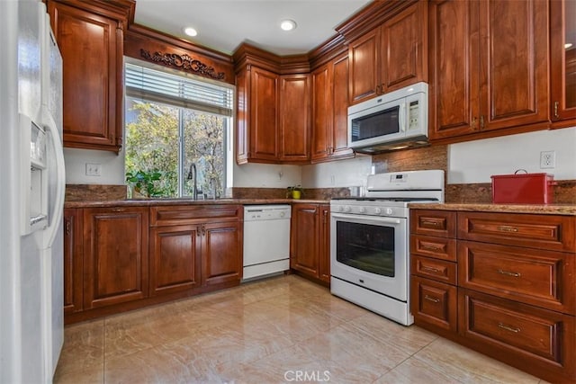 kitchen with a sink, white appliances, and dark stone countertops