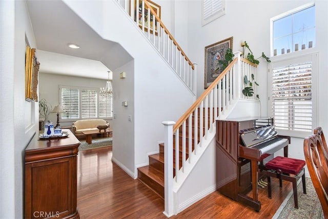 staircase with baseboards, an inviting chandelier, wood finished floors, and a towering ceiling