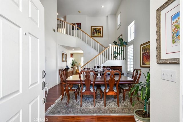 dining space with wood finished floors, baseboards, a high ceiling, arched walkways, and stairs