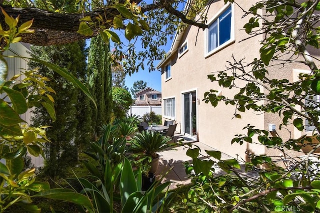 view of side of property with stucco siding, a patio, and fence