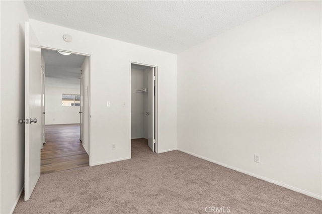 unfurnished bedroom featuring a walk in closet, a textured ceiling, a closet, carpet, and baseboards