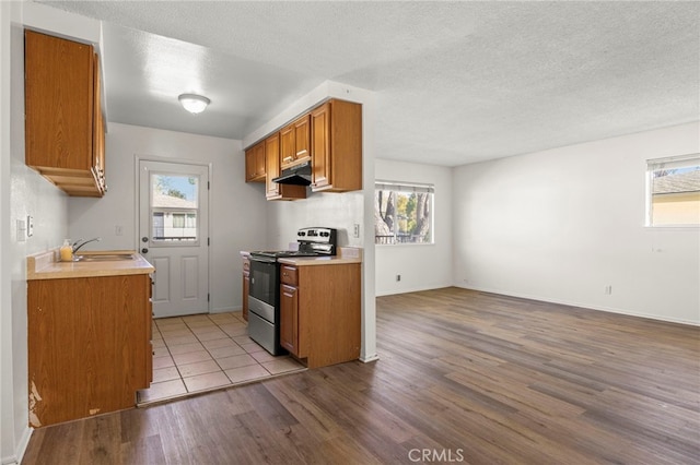 kitchen featuring a sink, light countertops, stainless steel range with electric stovetop, light wood-style floors, and brown cabinets