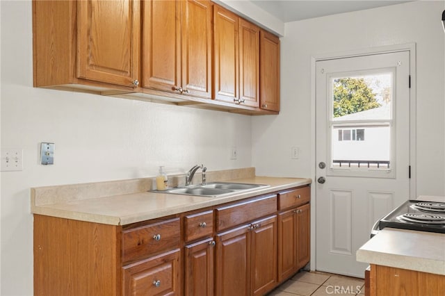 kitchen featuring light countertops, electric range oven, brown cabinets, light tile patterned flooring, and a sink