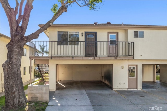 view of front facade featuring stucco siding, driveway, an attached garage, and stairs