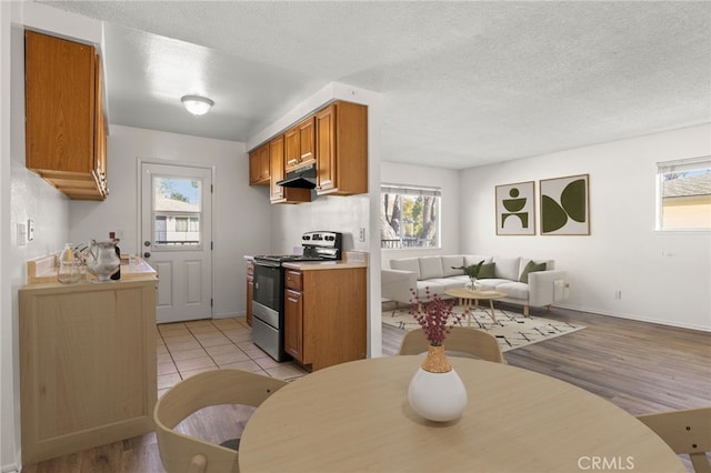 kitchen with under cabinet range hood, open floor plan, brown cabinets, stainless steel range, and a textured ceiling